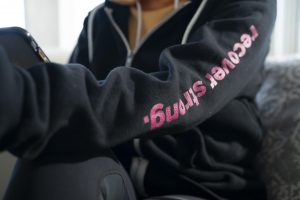 close up of sweatshirt that reminds customers to recover strong and for others to detect breast cancer symptoms early